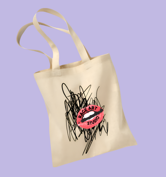 Beige canvas tote bag with black scribble in the background and the Rage Art Studio Lips logo in the foreground at an angle.