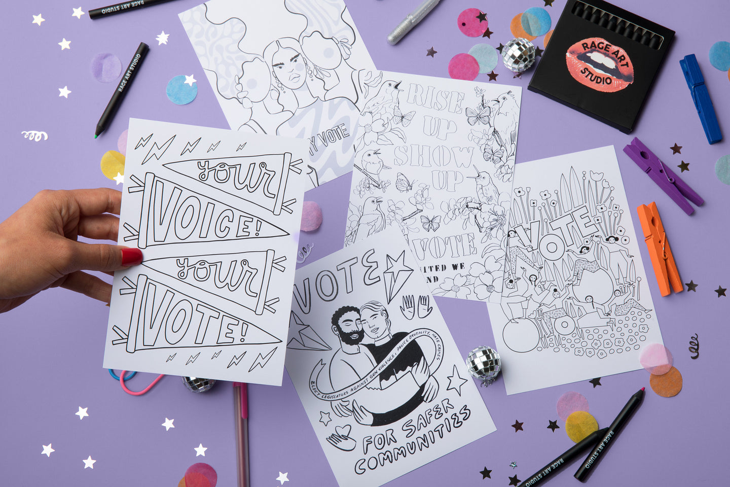 An alternate image of the 5 black and white postcards with the voting theme. A woman is holding one of the cards. The colored pencils are also pictured. The images pictured are: "Your Voice, Your Vote", "My Voice, My Vote, My Power," "Rise Up, Show Up, Vote," "Vote for Safer Communities" and "Vote".